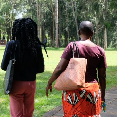 Two women walk through a green garden in a university campus with their backs to the camera.
