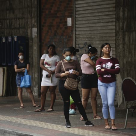 Women stand in line to enter a supermarket; some of them wearing a protective mask.
