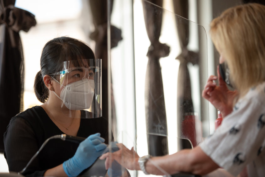 A manicurist wearing a face mask, face shield and gloves attends to a customer's nails.