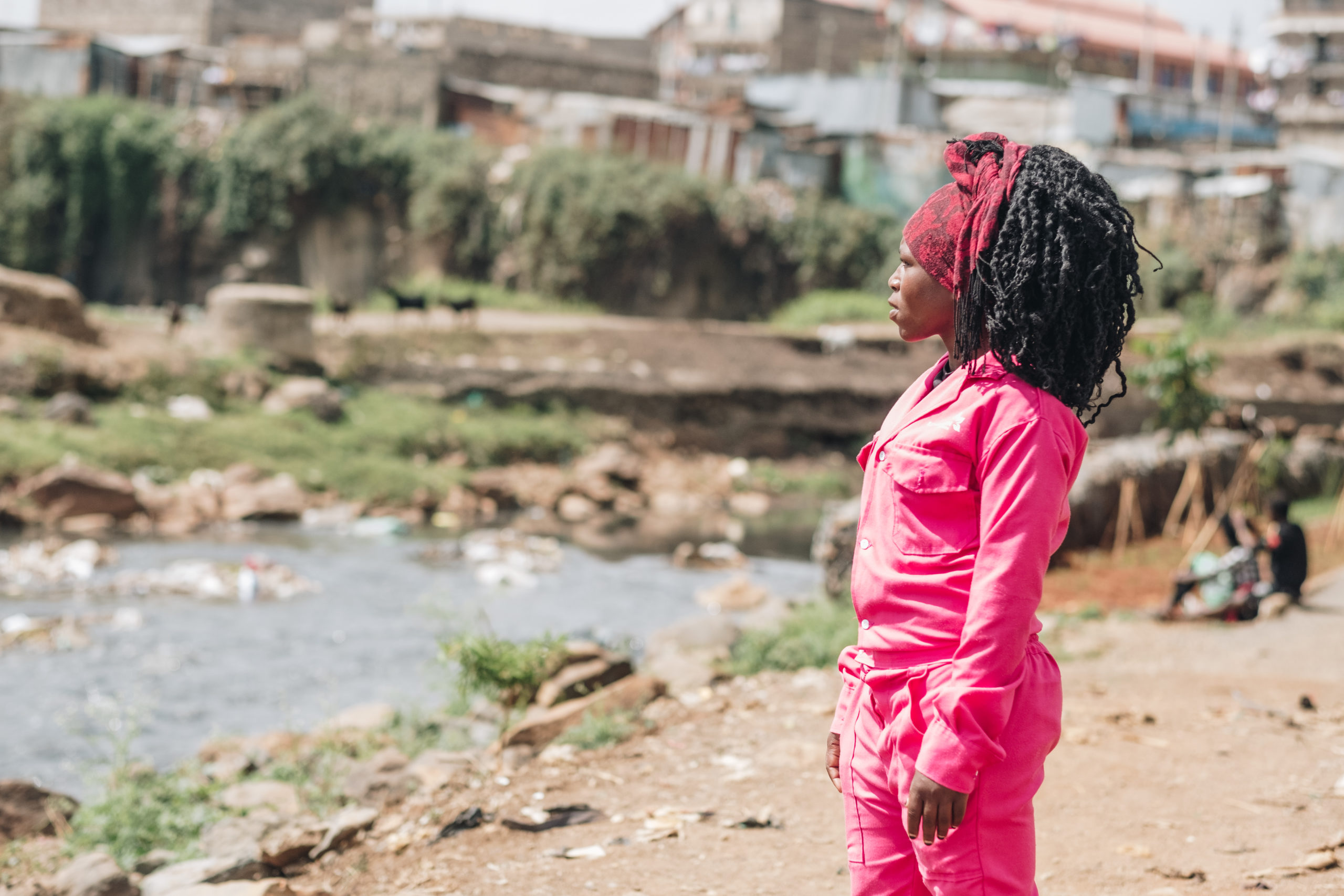A woman stands at a river bank looking toward the water