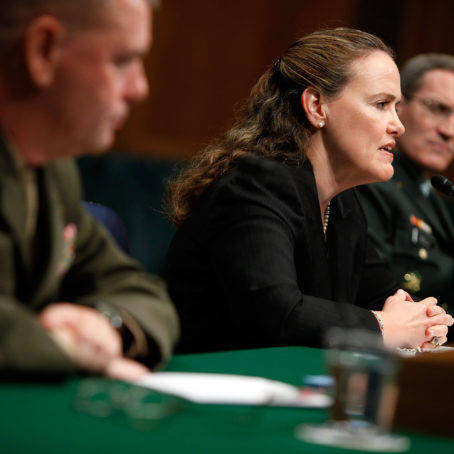 Image of two men and a woman seated at a table. The woman is speaking into a microphone