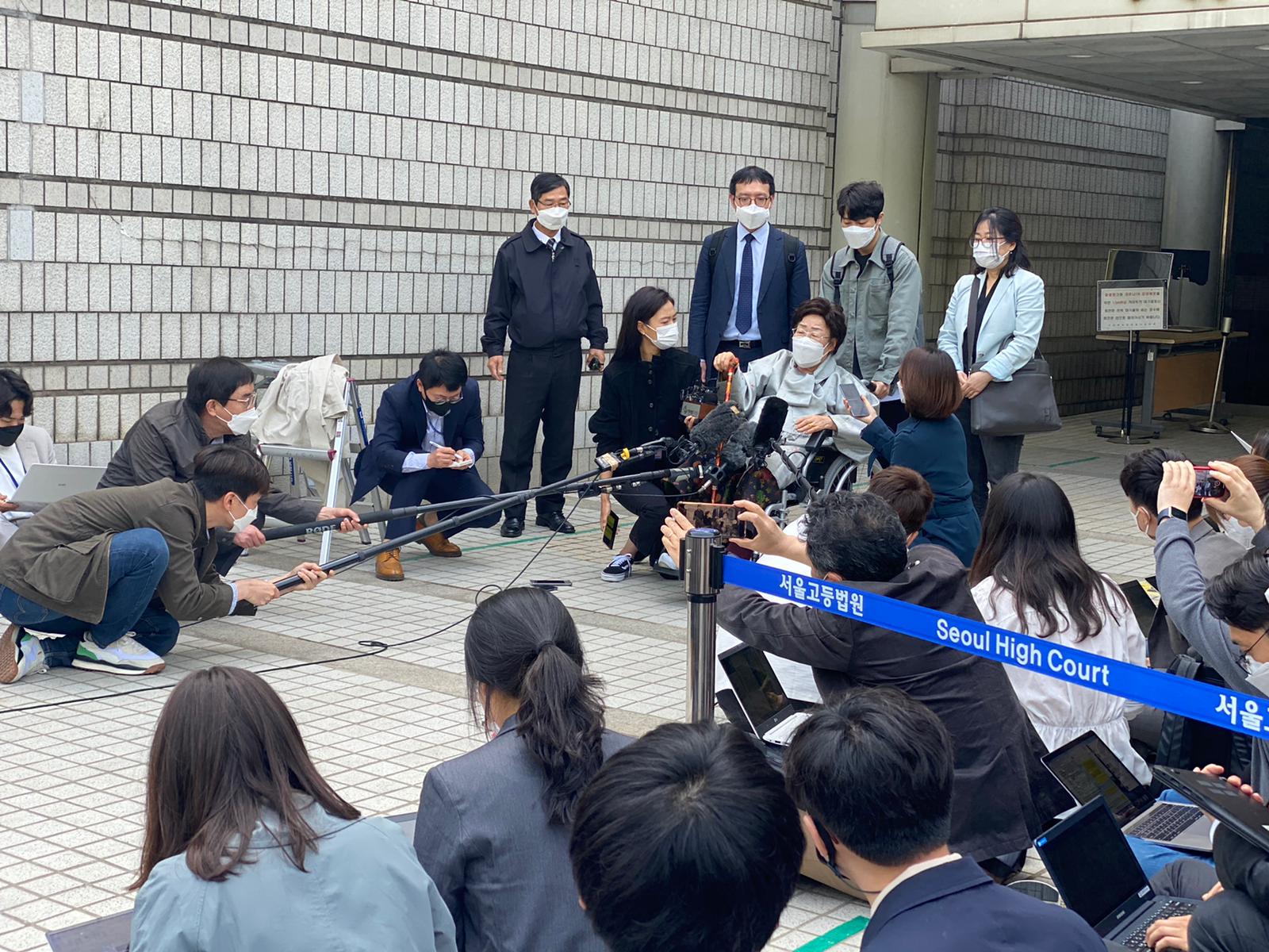 a woman exits a building where a crowd of gathered journalists waits
