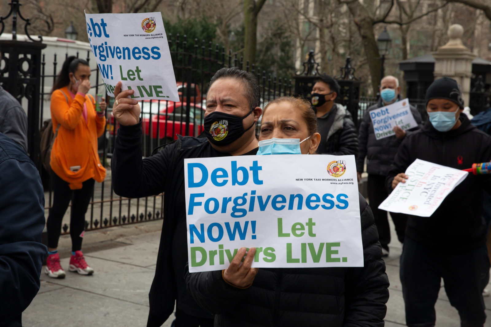 A photo of a group of people holding protest signs as they stand on a sidewalk