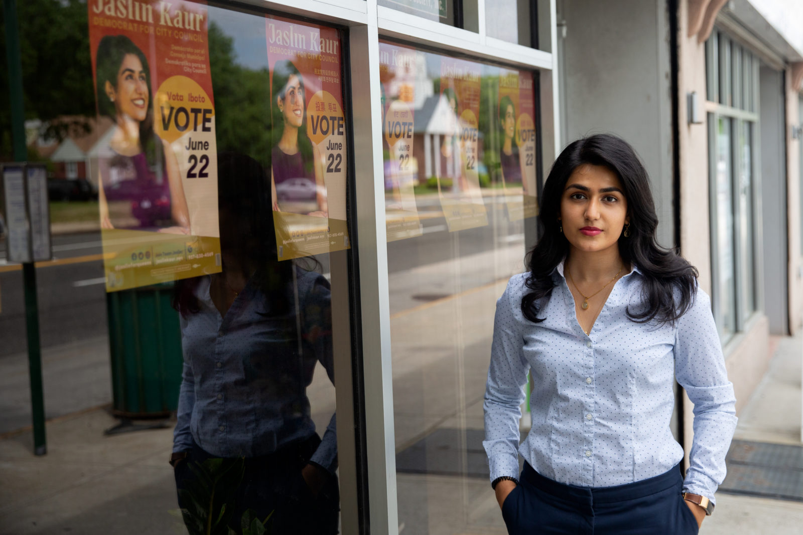 A photo of a woman standing on a sidewalk, next to a window