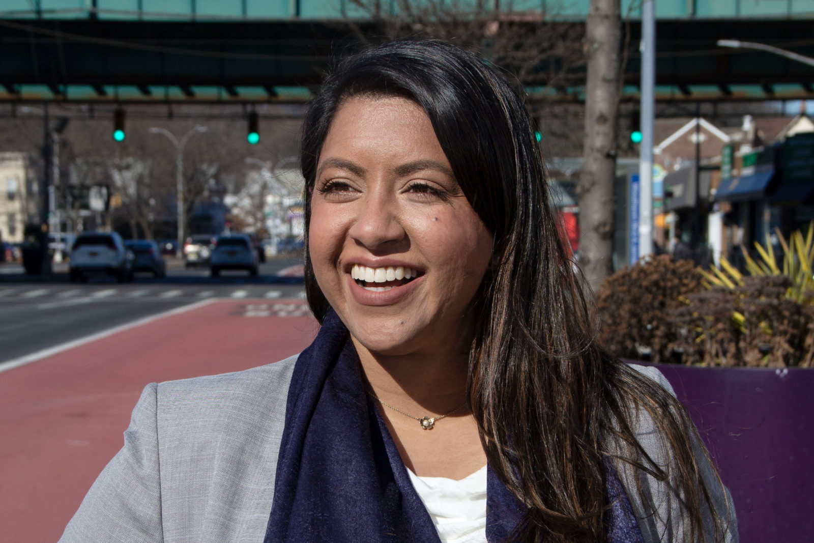 A photo portrait of a smiling woman standing outside along a city street