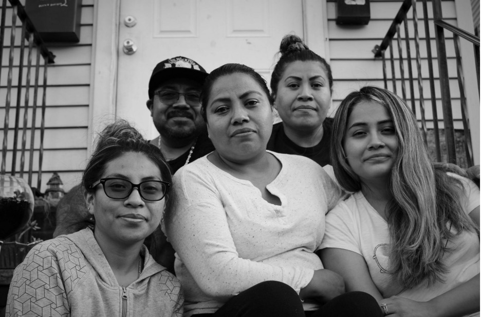 A black-and-white photo of a woman seated on a stoop, surrounded by family