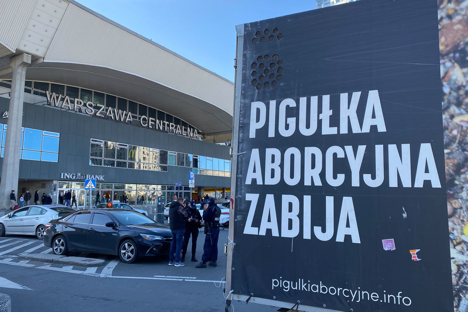 A photo of a truck with a sign in Polish parked outside of a train station