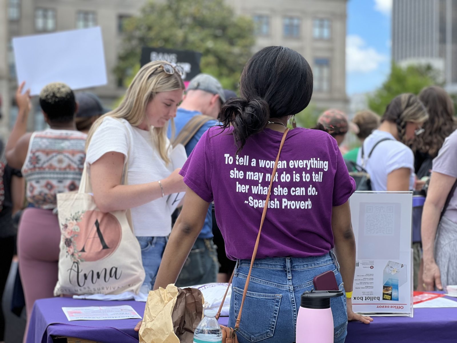 A woman stands at a table handing out information cards.