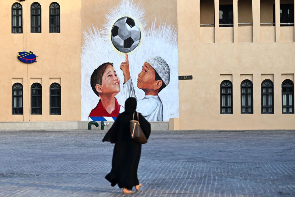 A woman walks past a mural of two boys looking up at a soccer ball.