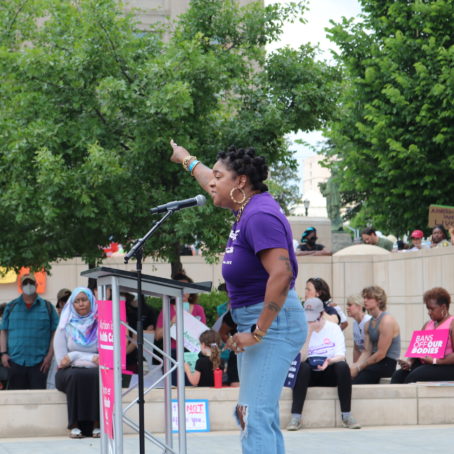 A woman stands at a podium and points at the Georgia statehouse building.