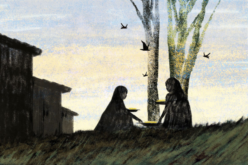 Two women sit on grass in front of a tree.