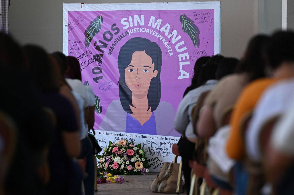 A portrait of a woman's (Manuela) face sits in front of a group of people sitting down.