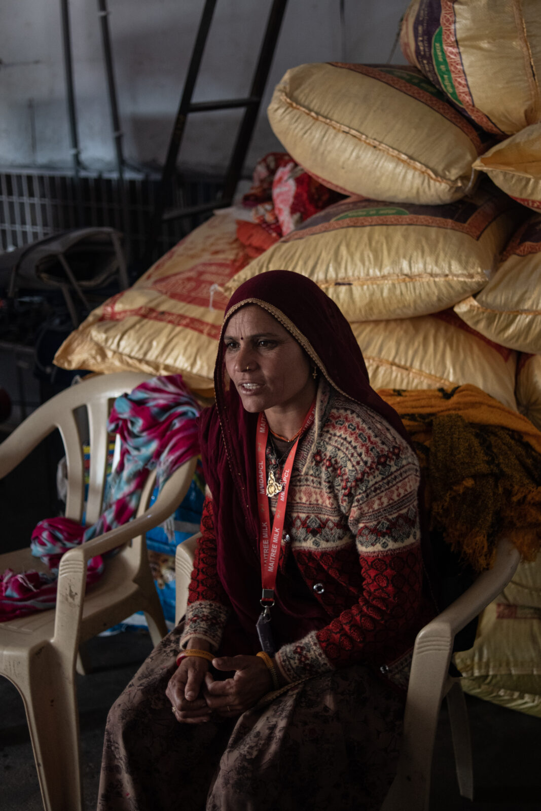 A woman sits in a white chair with brown bags piled behind her. 