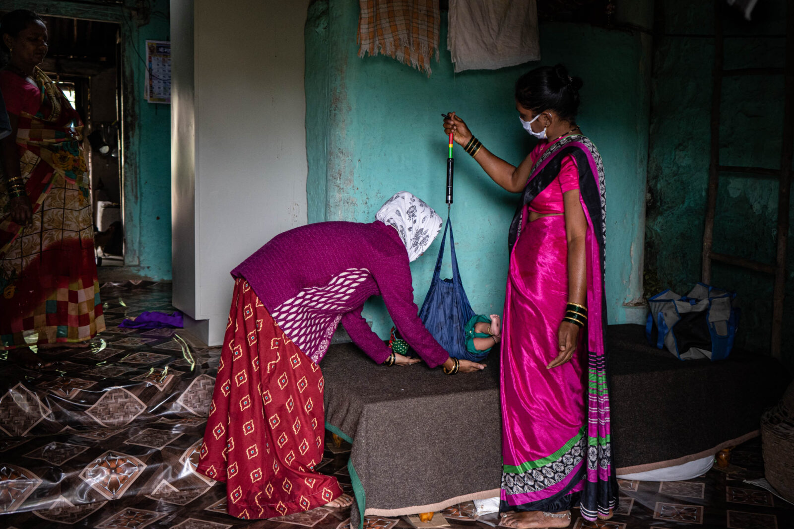 Two women stand while weighing a baby.